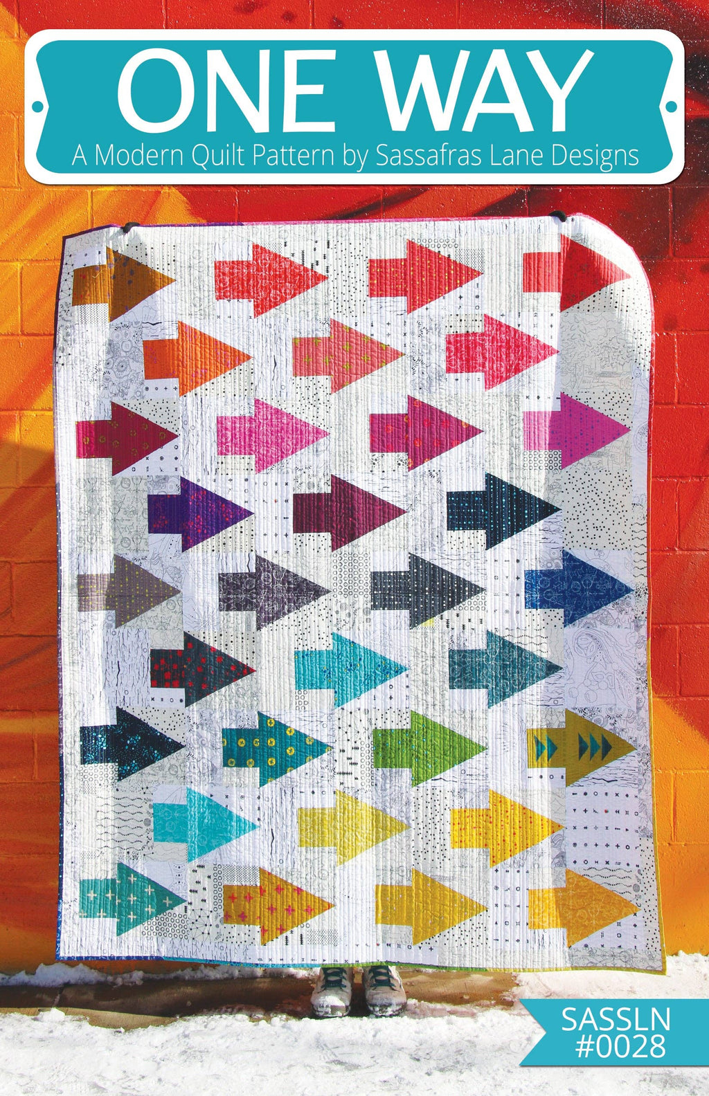 A quilt with a geometric arrow pattern in multiple colors displayed against a red background.