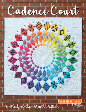 A colorful quilt displayed against a brick wall background, with a title 'Cadence Court' written on it, indicating it is a pattern book for making the quilt.