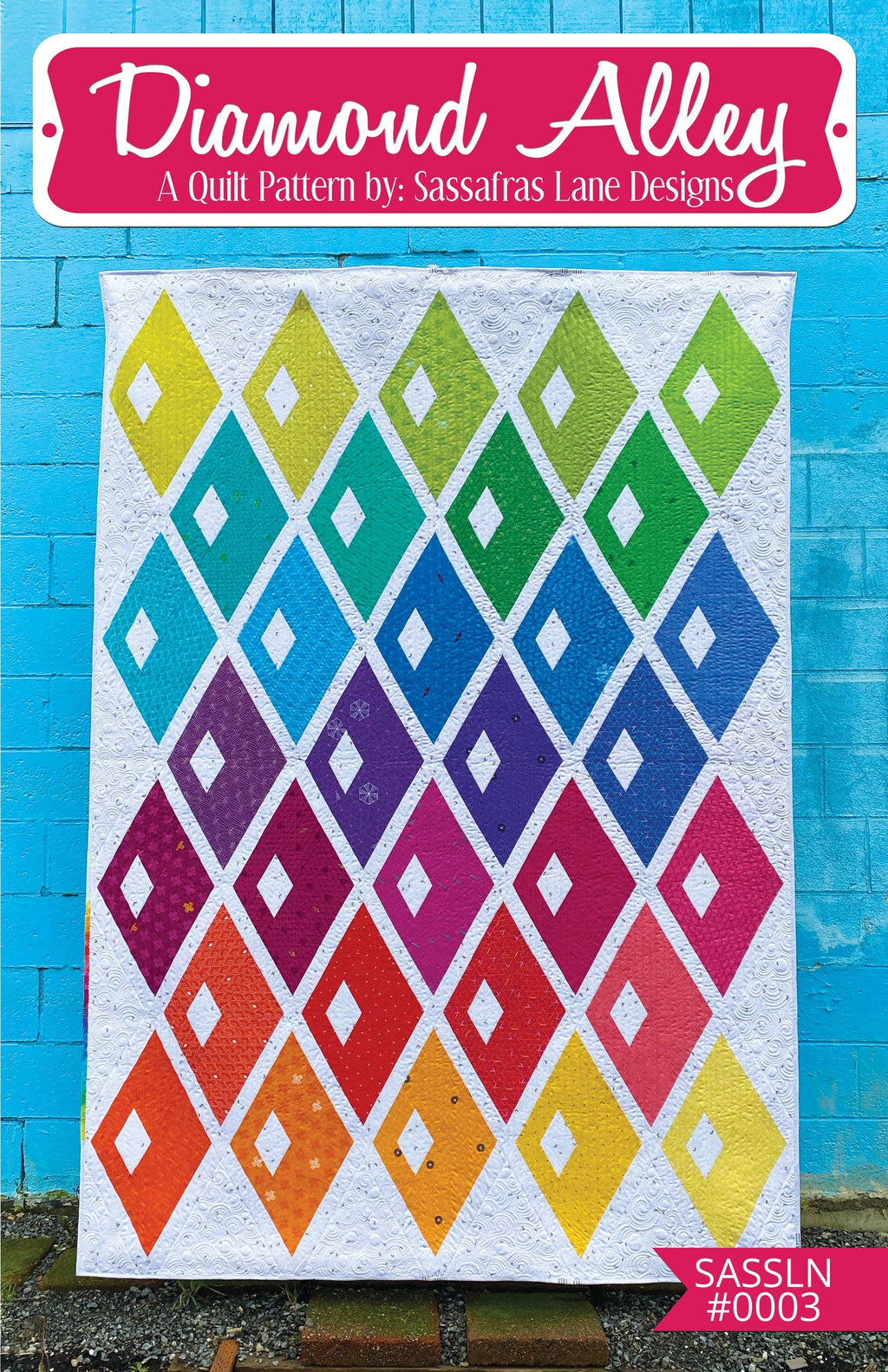 A colorful diamond-shaped quilt pattern displayed against a blue wall, with the text 'Diamond Alley A Quilt Pattern by Sassafras Lane Designs' at the top.