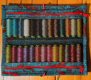 Set of colorful thread spools in a blue case with red zipper on a wooden surface