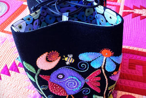 Colorful embroidered bag with floral and bird designs on a patterned fabric background