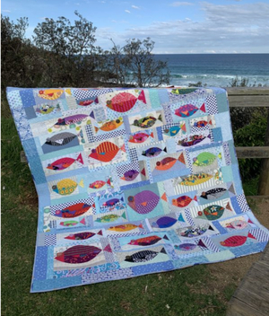 Colorful fish-patterned quilt on a grassy area with ocean view