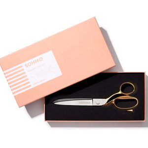 Gold scissors in a black box with a pink box labeled 'GOMMO' on a white background