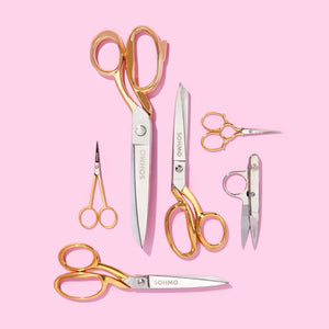 Set of gold-handled scissors on a pink background