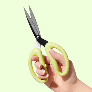 Hand holding a pair of green scissors against a light green background