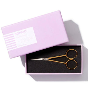 Pair of gold scissors in a pink box with 'SOMNO' branding on a white background