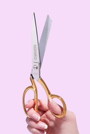 Hand holding a pair of scissors with a pink background