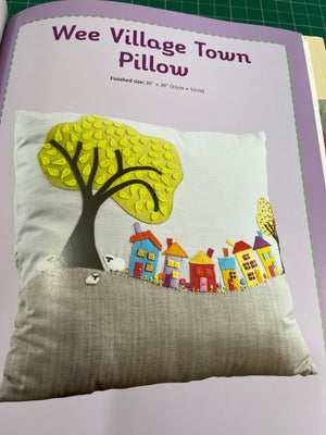 Decorative pillow with colorful houses and a yellow leaf design on a gray background.